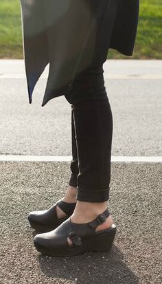 A woman wearing black plantar fasciitis shoes and a black dress stands on the road