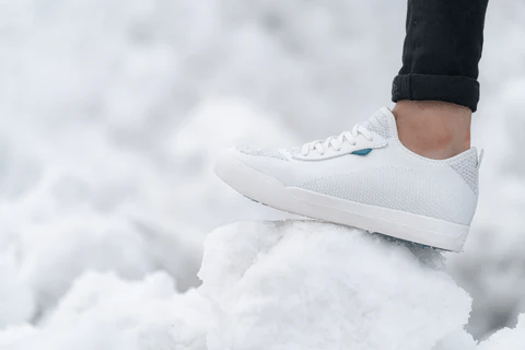A man wearing white sneaker standing on a snow piece 